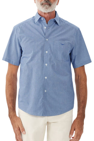 A person with a white beard is wearing an RM Williams Hervey short-sleeve shirt, featuring a button-up blue design with a small checkered pattern. Made from breathable cotton, the shirt includes a collar, a chest pocket on the left side, and white buttons. The person is also wearing light-colored pants against a plain white background.