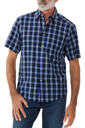 A person is wearing the RM Williams Hervey Shirt, a short-sleeve, button-up shirt featuring a blue and black plaid pattern. The breathable cotton fabric drapes comfortably over their frame, showing a relaxed silhouette. They have a white beard and are also wearing blue jeans. The background is plain white.