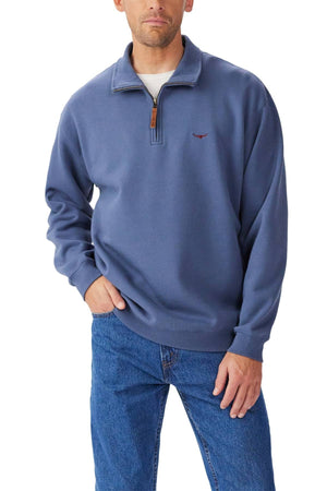 A man in the RM Williams Mulyungarie 1/4 Zip Sweatshirt—blue, organic cotton, small chest logo—and blue jeans stands with one hand in his pocket against a white background.