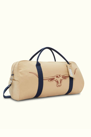 The RMW Nanga Canvas Bag is a beige duffel-style bag with dark blue straps and a longhorn symbol on the side. This versatile bag has a side zipper and includes a small luggage tag.
