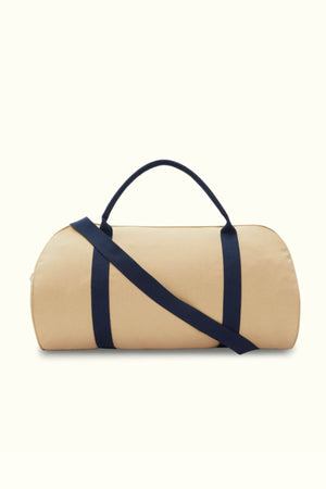 The RMW Nanga Canvas Bag, featuring a versatile duffle-style design, comes in beige with dark blue handles and a matching shoulder strap, presented on a plain white background.