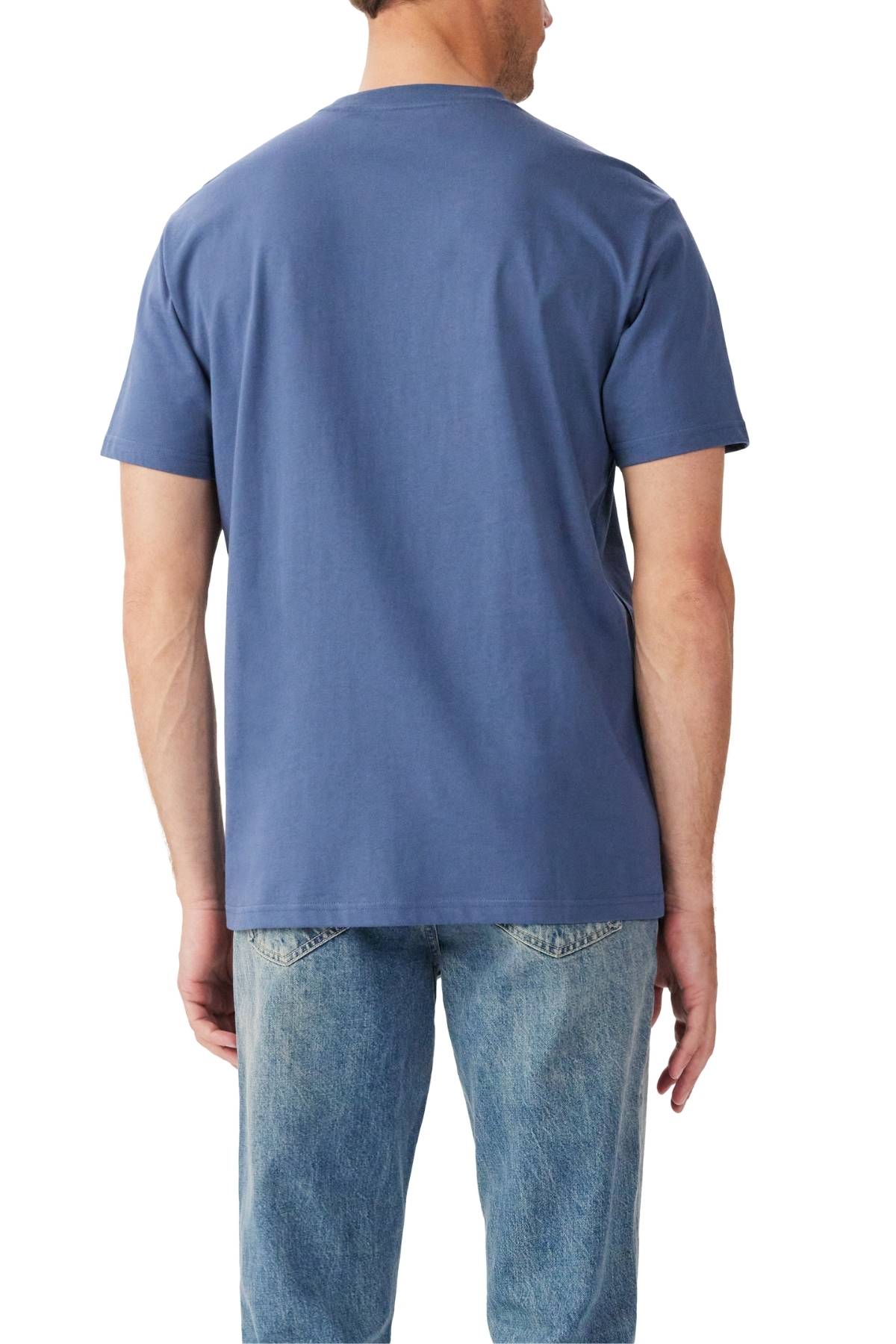 A man faces away from the camera, wearing an RM Williams Parson T-Shirt in plain blue with short sleeves and a ribbed crew neck, paired with light blue jeans against a white background.
