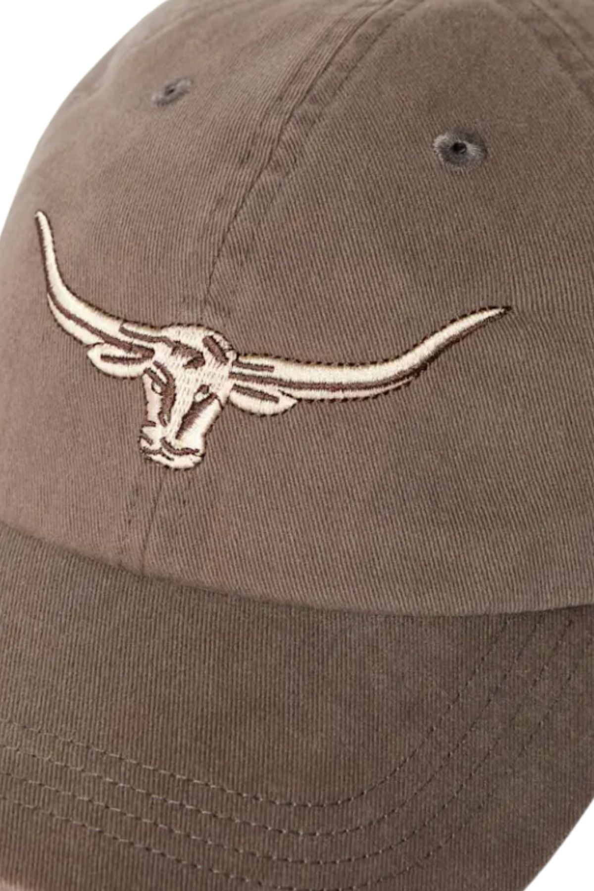A close-up of the RM Williams Longhorn Twill Cap shows an embroidered steer’s head on organic cotton, with visible stitching, ventilation eyelets, and an adjustable strap for comfort.