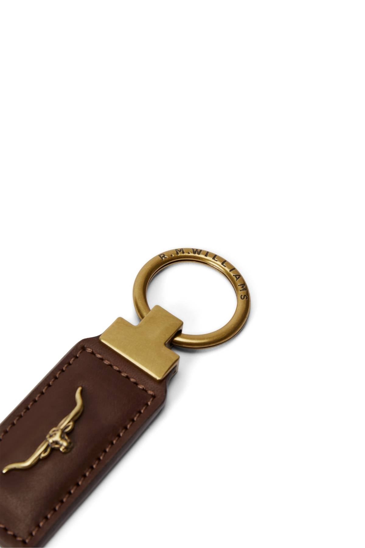 A close-up of the RM Williams Angaston Key Fob, a brown leather keychain with gold hardware, featuring an embossed bull logo and "R.M.Williams" engraved on the split keyring against a white background.