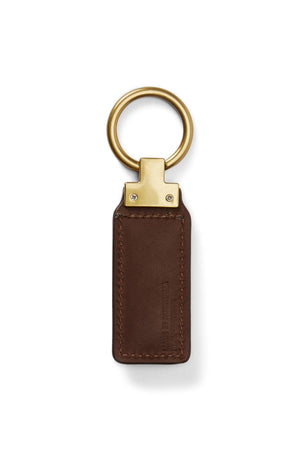 The RM Williams Angaston Key Fob is a brown leather keychain with a rectangular tag, featuring visible stitching, a large split keyring, and metallic detailing where the ring attaches to the leather.
