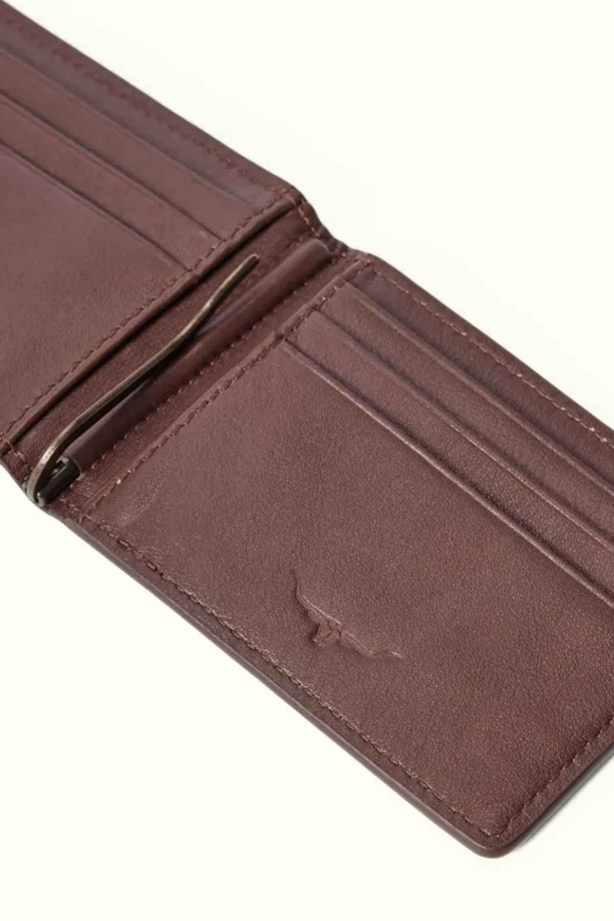 The RM Williams Farrier Bi Fold Wallet, crafted from premium brown leather, lies on a light surface. It features multiple card slots, a modern money clip, and a subtle embossed design on the lower part.