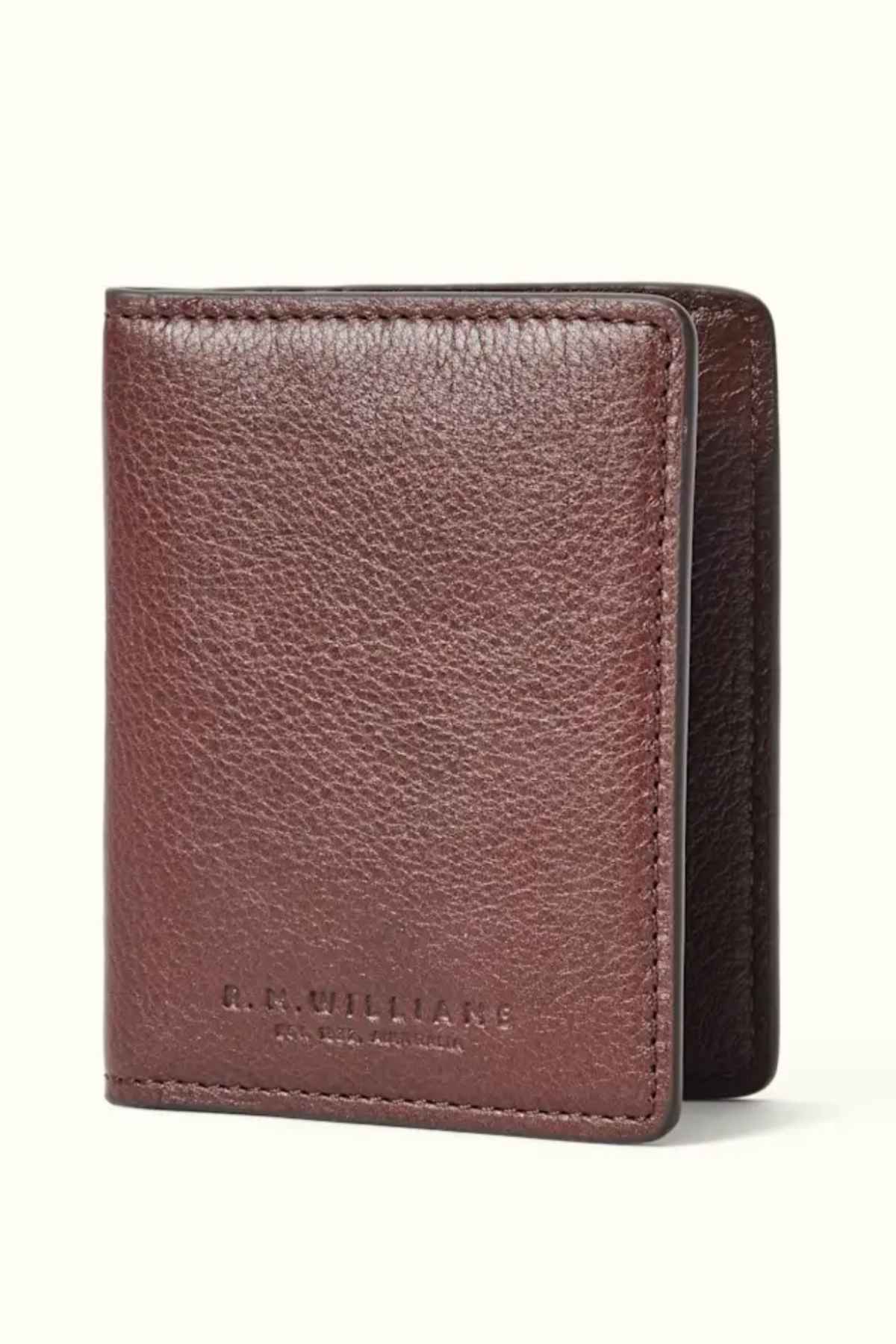 An RM Williams Farrier Fold Cardholder in brown premium leather stands upright on a light background, featuring a stitched edge and "R.M. Williams" embossed on the front. Its textured finish complements the card slots, blending style with functionality.