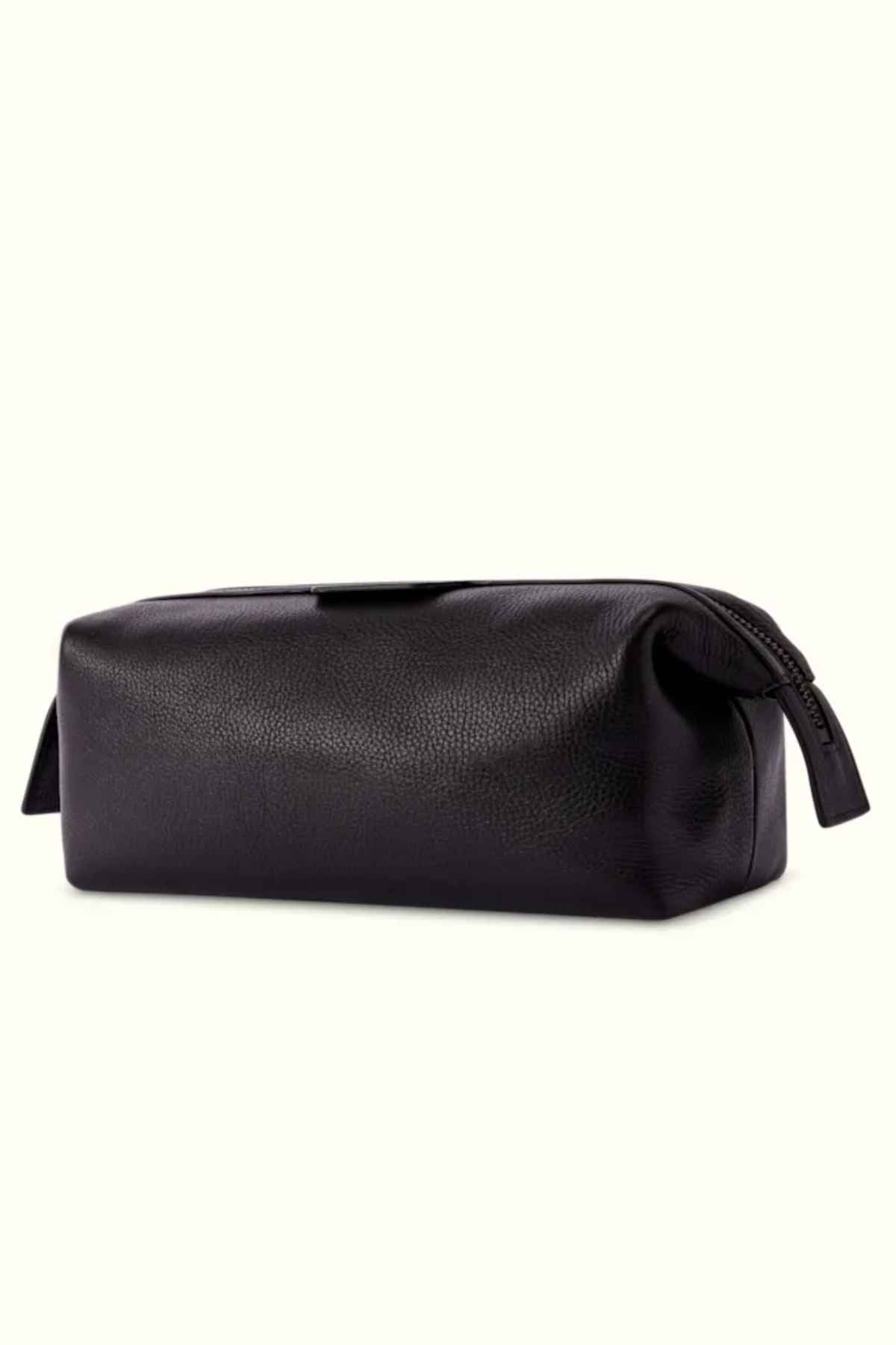 A close-up of the RM Williams Farrier Washbag, featuring a black leather finish with a frog-mouth zipper. The rectangular-shaped bag showcases slight texture on the leather, set against a plain cream background.