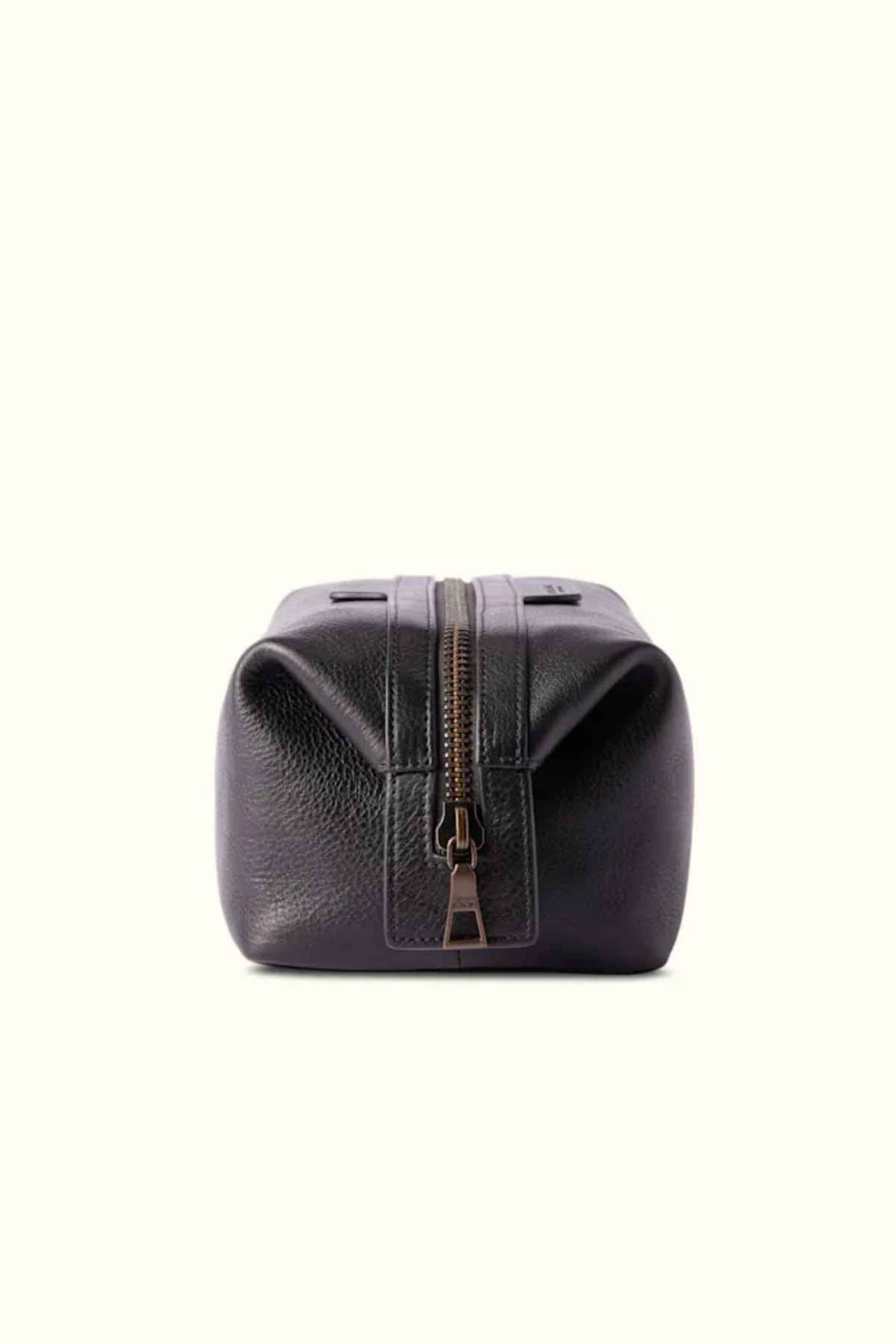 The RM Williams Farrier Washbag, crafted from black leather with a frog-mouth zipper, is displayed against a light background. It stands upright with its zipper slightly open, highlighting its textured surface and structured design.