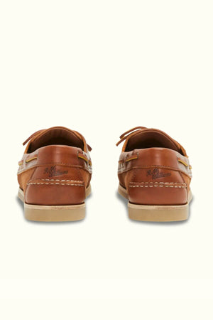 Two RM Williams Hobart Boat Shoes in brown bovine leather, viewed from the back, showcase beige soles and stitching. The brand name is visible on each heel, making them perfect for casual wear.