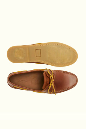 Top and bottom views of the RM Williams Hobart Boat Shoe in casual brown bovine leather with tan laces, featuring a sole tread pattern, white toe stitching, and subtle yellow side accents.