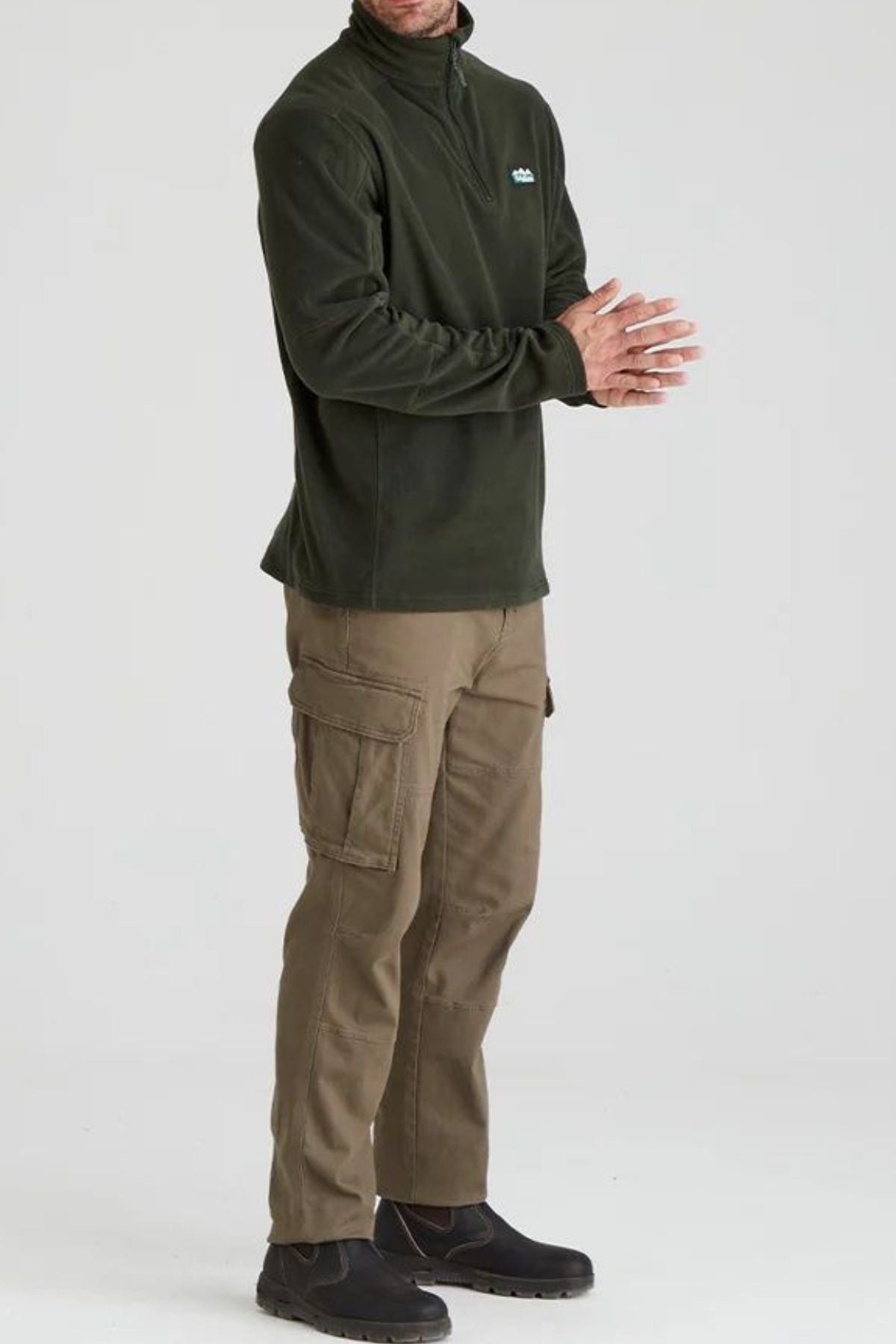 A man with his arms loosely crossed models the Ridgeline Narvik Fleece in olive green, paired with khaki cargo pants and black shoes against a plain background. His face remains unseen.