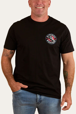 A smiling man stands with one hand in his pocket, wearing the Ringers Western Bucking Bull Loose T-Shirt in black with a small circular logo on the left chest, paired with light blue jeans.