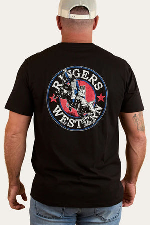 Man wears the Ringers Western Bucking Bull Loose T-Shirt, featuring a cowboy riding a bull graphic, “Ringers Western” text, and red stars on the back. He completes the classic Western look with a beige and white cap.