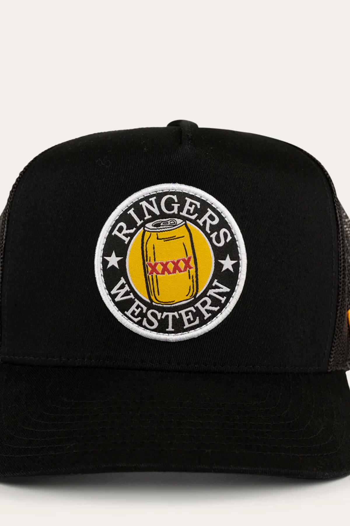 The Ringers Western Can Trucker cap includes a black twill front with an off-white patch showcasing a yellow can and red "XXXX" text, encircled by "Ringers Western." Its poly mesh back ensures breathability for all-day comfort.