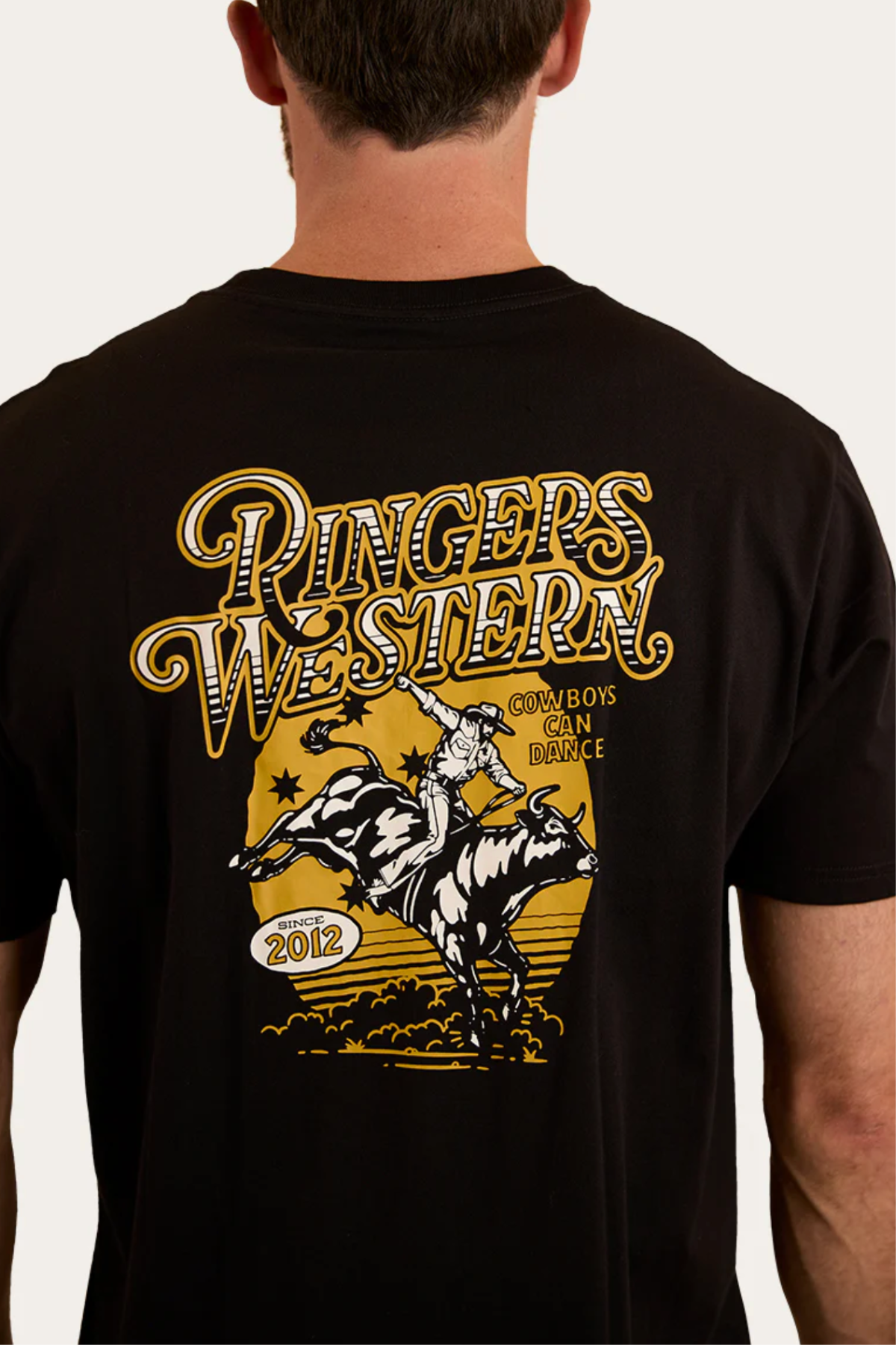 Wearing a Ringers Western Cowboys Can Dance Loose Fit T-Shirt in black with a yellow and white cowboy-on-bull graphic and bold "Cowboys Can Dance" text, plus "Since 2012.