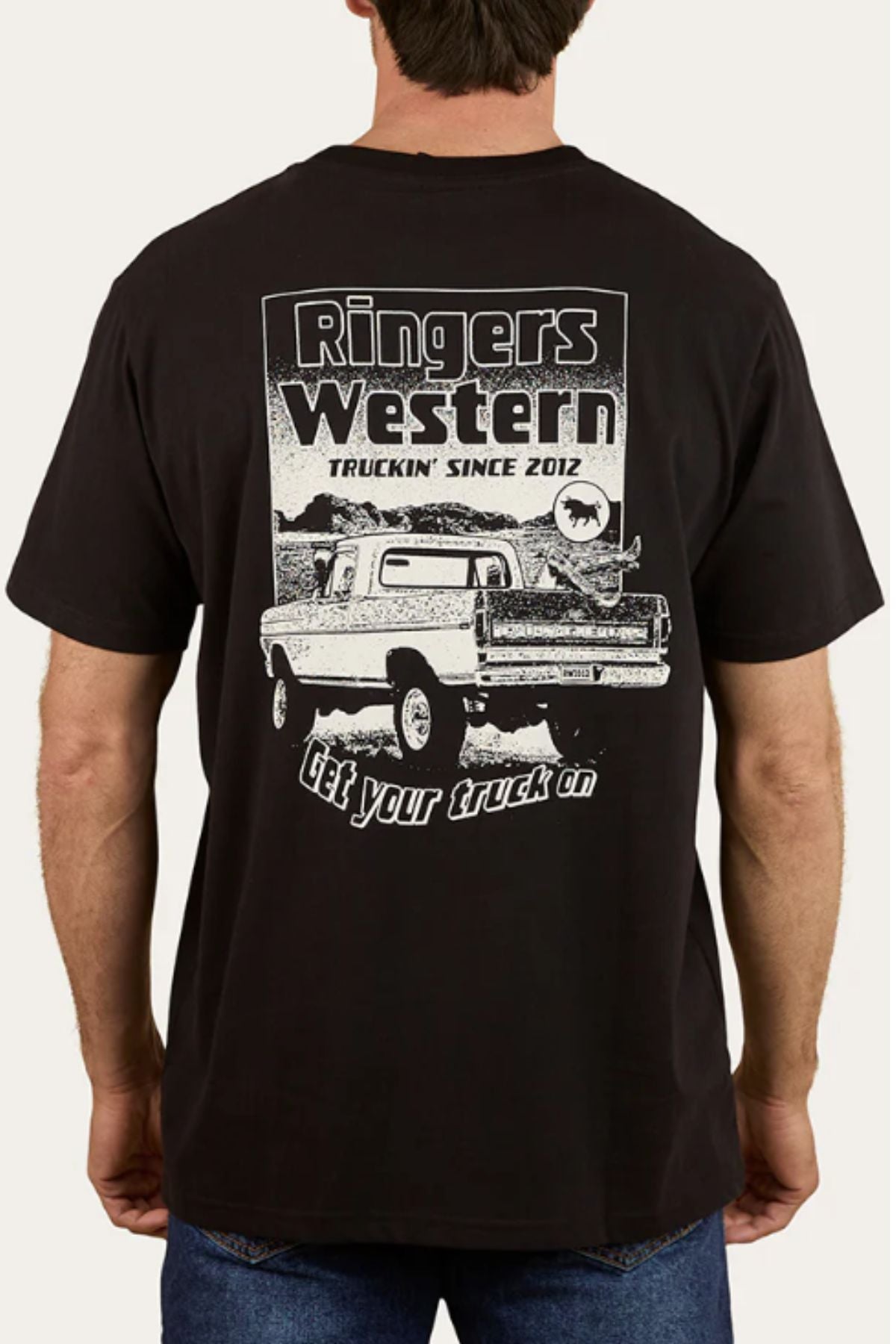 A man wears the Ringers Western Get Your Truck On Loose Fit T-Shirt, made from 100% cotton, with a bold pickup truck graphic and "Truckin' Since 2012. Get your truck on." printed on the back.