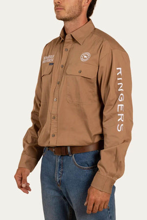 A person wearing a Ringers Western Hawkeye Embroidered Shirt, a brown long-sleeve shirt with "Ringers Western" embroidered on the chest and sleeve. The premium cotton shirt features chest pockets and is neatly tucked into blue jeans, secured with a brown belt. The background is plain white.
