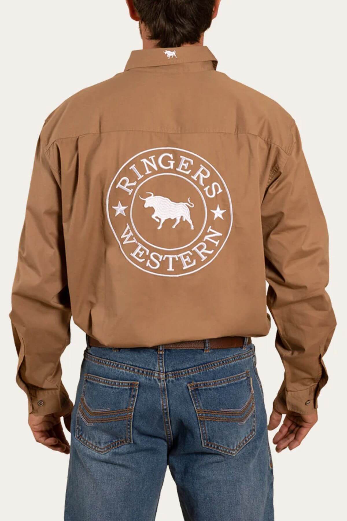 A person wearing a light brown Ringers Western Hawkeye Embroidered Shirt, crafted from premium cotton and featuring a logo on the back that encircles an illustration of a bull. The shirt provides UPF 50+ sun protection and is tucked into blue jeans. The person is facing away from the camera.