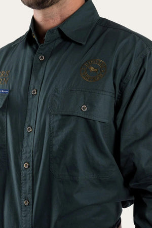 A person wears a Ringers Western Hawkeye Embroidered Shirt in dark green, made of premium cotton with an emblem and text patch on the chest. It features button-up style, visible stitching, and buttoned chest pockets; their face isn't visible.
