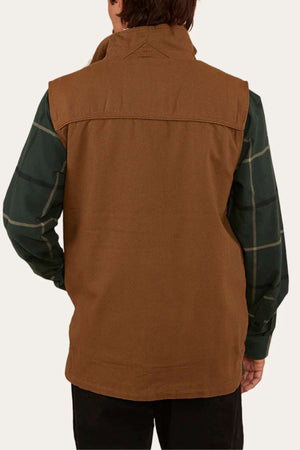 A person facing away wears the Ringers Western High Country Vest in brown cotton canvas over a green plaid long-sleeve shirt and black pants, against a plain light-colored background.