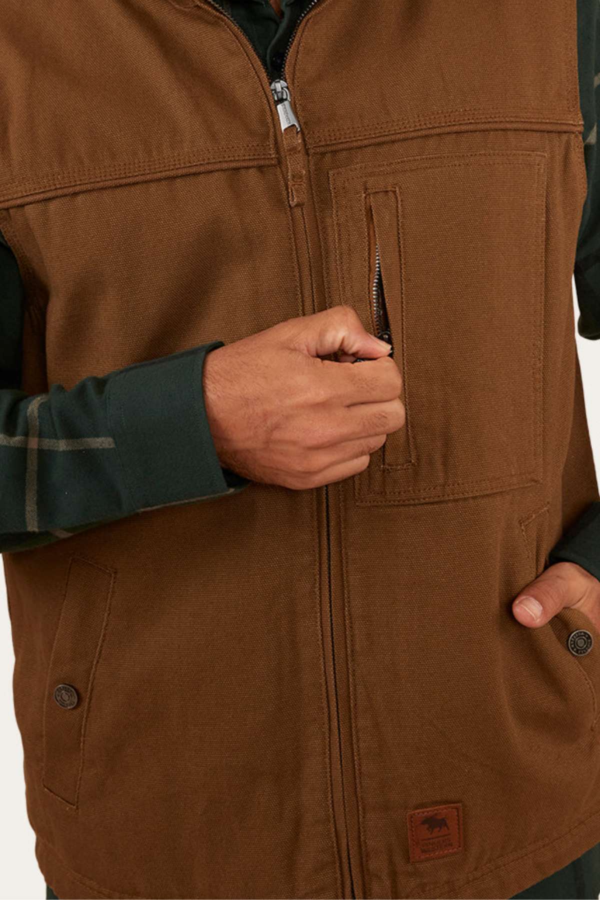 A person wearing the Ringers Western High Country Vest over a dark green shirt is unzipping a vertical chest pocket on the vest. Only their torso and hand are visible.