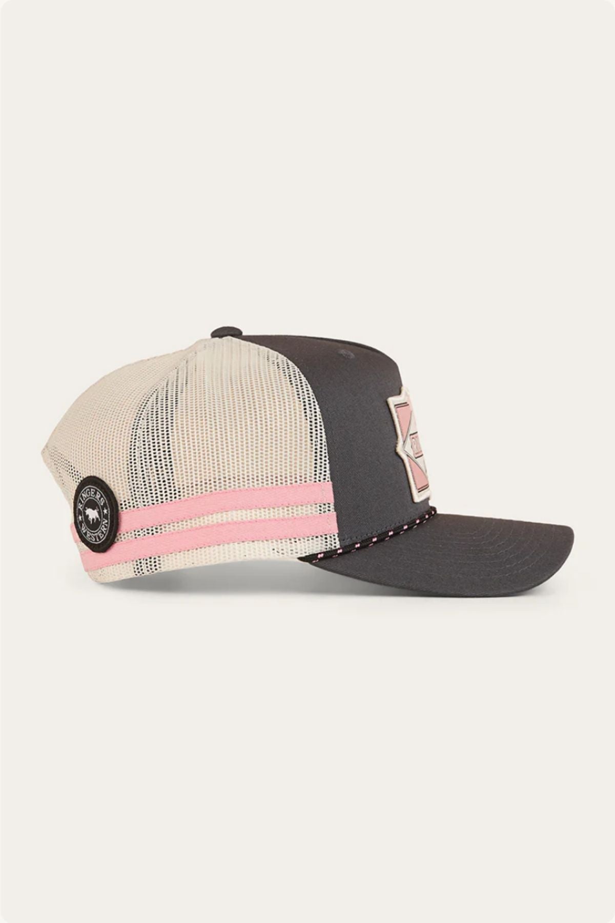 The Ringers Western Hometown Trucker Cap has a dark gray bill and front, cream mesh back, pink and white stripes, a round black side patch, a geometric front patch, and an adjustable snapback.