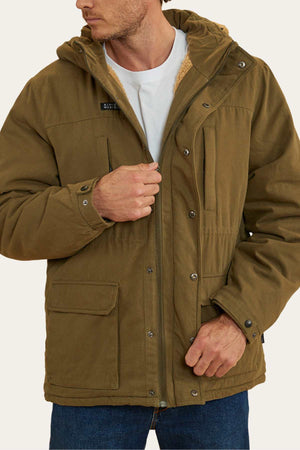 A man wearing a green Ringers Western Judd Jacket, which features multiple pockets, is seen adjusting the zipper. He is also sporting a white T-shirt underneath and blue jeans. The thick jacket, ideal for cold weather, boasts a cozy sherpa lining and a removable hood. The background is plain beige.