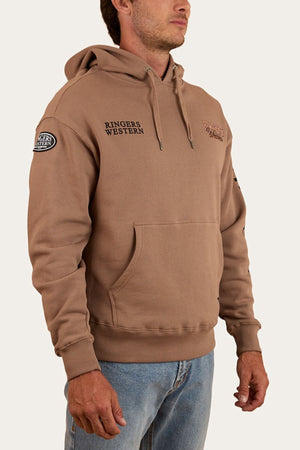 A man stands with arms relaxed, wearing the Ringers Western KNX Oversized Hoodie in brown with chest and sleeve logos, paired with light blue jeans against a plain background.