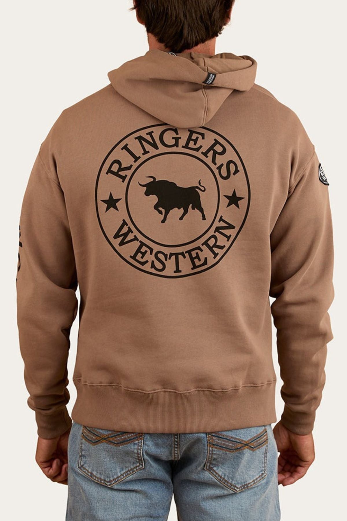 Someone is wearing the Ringers Western KNX Oversized Hoodie, featuring a large circular logo and bull graphic on the back, made from soft brushed fleece, and paired with blue jeans.