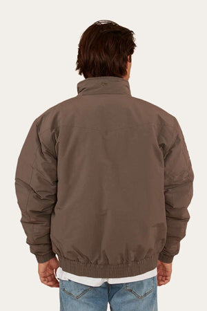 A person with short brown hair is seen from the back wearing a Ringers Western Kidman Jacket, characterized by its brown color, high collar, ribbed cuffs, and quilted lining—ideal for an outdoor adventure. They are also wearing light blue jeans. The background is plain and light-colored.
