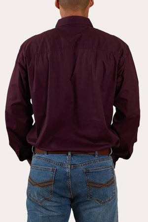 A person is pictured from behind wearing the Ringers Western King River Half Button Shirt in a dark maroon color and blue jeans. The image focuses on the upper back and rear view, highlighting the details of the comfortable, hard-wearing work shirt and jeans against a plain background.