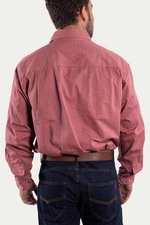 A man with short dark hair stands facing away, wearing a long-sleeved Ringers Western King River Half Button Shirt in red, tucked into dark blue jeans. The 100% cotton shirt features buttoned cuffs, and he is accessorized with a dark brown belt. The background is plain and light-colored.
