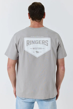A man is wearing the Ringers Western New Squadron Loose Fit Tee, made from 100% cotton in light gray. The back of the shirt features “RINGERS WESTERN” in bold letters, along with a small bull head graphic and the text “EST 2012.” He is facing away from the camera.