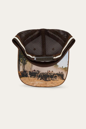 The Ringers Western Pendleton Trucker Cap is shown from beneath, highlighting the inside of the brim, which features a detailed image of men racing wooden canoes on a river with trees and bushes in the background. It comes with an adjustable snapback to ensure a perfect fit for everyone.