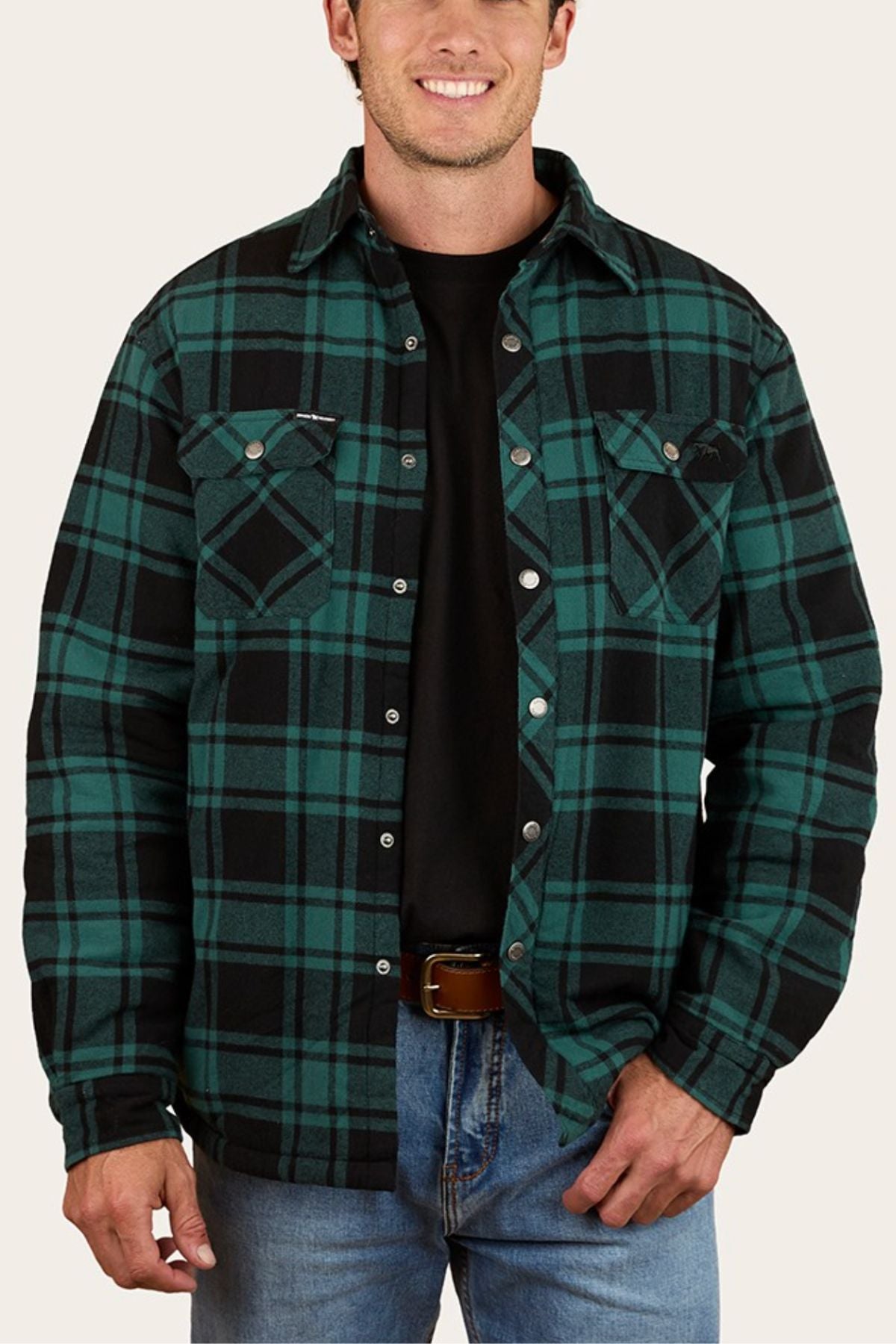 A man smiles while facing forward, wearing the Ringers Western Sawyer Flannel Shirt over a black t-shirt and blue jeans, with his hands resting casually near his pockets.