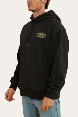 A person is wearing a black Ringers Western Servo Hoodie with an oversized fit, featuring a small yellow and green logo on the left chest that reads "Fingers Crossed." They are also wearing light blue jeans. The background is plain white.