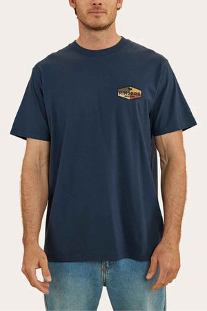 A person is wearing a Ringers Western Servo Loose Fit T-Shirt in navy blue, crafted from 100% cotton jersey, paired with blue jeans. The shirt features the brand's logo on the left chest against a plain off-white background.