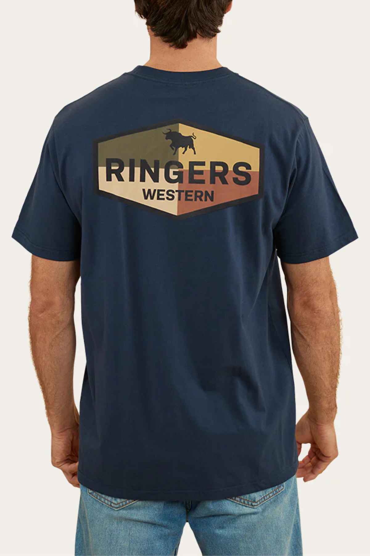 The individual is wearing a Ringers Western Servo Loose Fit T-Shirt, made from 100% cotton jersey in a dark blue hue featuring a cattle graphic on the back. Combined with blue jeans, this loose fit provides comfort and style.