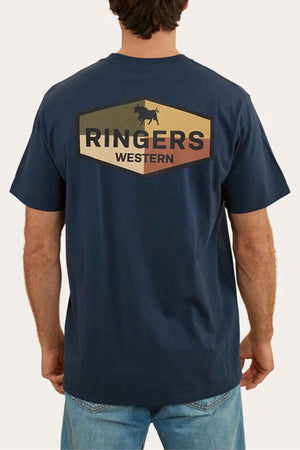 The individual is wearing a Ringers Western Servo Loose Fit T-Shirt, made from 100% cotton jersey in a dark blue hue featuring a cattle graphic on the back. Combined with blue jeans, this loose fit provides comfort and style.