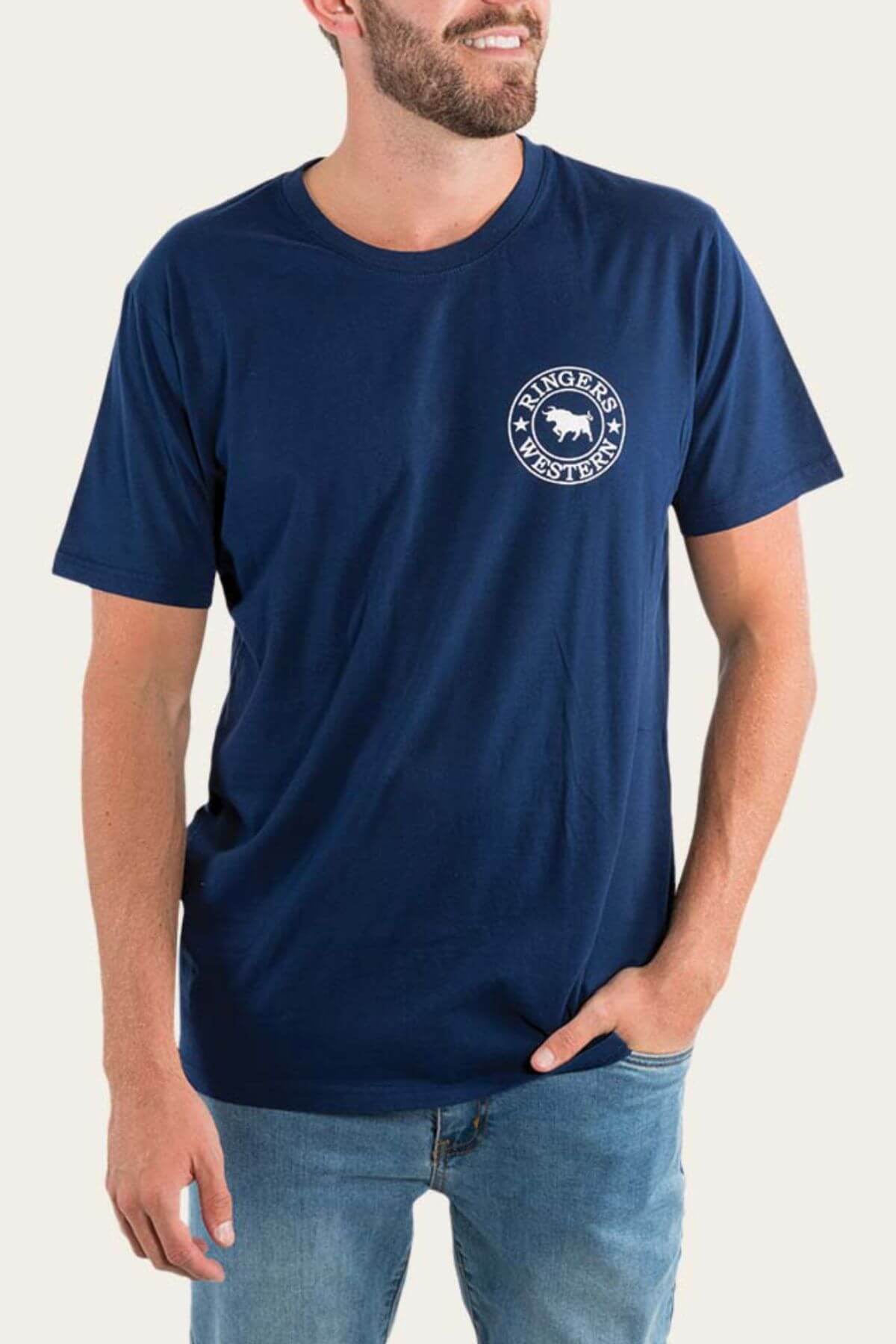 A bearded man smiles slightly in a blue Ringers Western Signature Bull Loose Fit T-Shirt made from soft cotton jersey, perfectly complementing his relaxed pose with one hand casually in his jeans pocket.