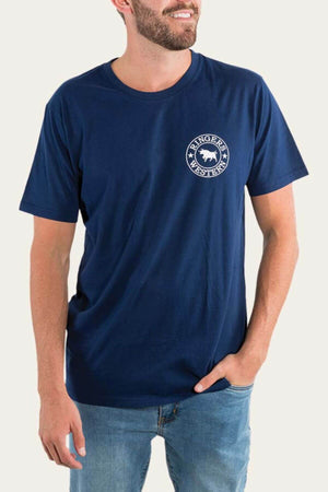A bearded man smiles slightly in a blue Ringers Western Signature Bull Loose Fit T-Shirt made from soft cotton jersey, perfectly complementing his relaxed pose with one hand casually in his jeans pocket.