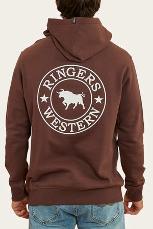 A person wearing a comfortable Ringers Western Signature Bull Pullover Hoodie in brown, featuring "Ringers Western" and a bull graphic printed on the back. The individual is standing with their back facing the camera, showcasing the design, paired with blue jeans.