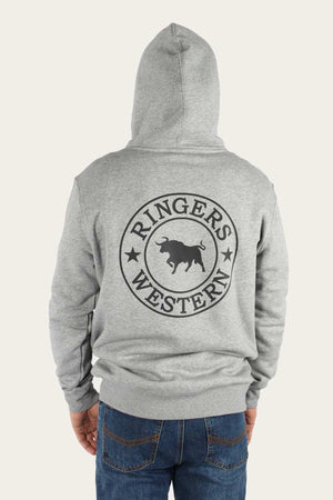 A person wearing a light gray Ringers Western Signature Bull Pullover Hoodie with a large black logo on the back. The logo features the text "Ringers Western" circled around the silhouette of a bull, flanked by two stars. This comfortable hoodie pairs perfectly with their blue jeans, creating a relaxed and stylish outfit.