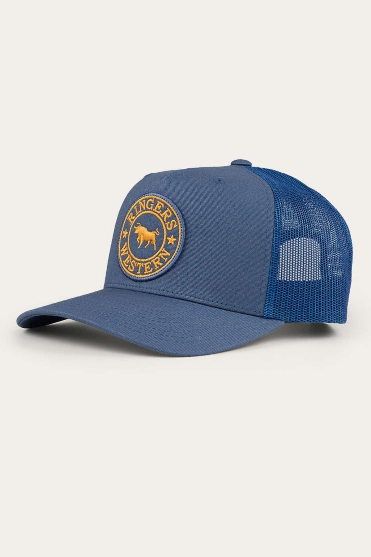 The Ringers Western Signature Bull Trucker Cap is a blue trucker hat featuring a round patch on the front panel with an image of a bull and the words "Ringers Western" in a circular design. It has a cotton twill peak, standard bill, breathable mesh back, and Snapback closure for easy adjustment.