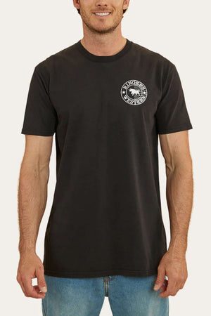 A person stands wearing a black short-sleeve Ringers Western Signature Flag Stock Fit T-Shirt crafted from 100% cotton jersey, showcasing a small, circular logo on the left chest featuring a wolf and the text "WOLVERINE RANCH" around the edge. The person is also wearing blue jeans. The background is plain white.