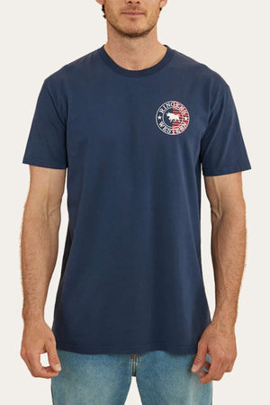 A man wearing a navy blue Ringers Western Signature Flag Stock Fit T-shirt, made from 100% cotton, featuring a circular logo on the left chest area with a red, white, and blue design and the text "Ranger USA Nest Fest." He has light skin and short, dark hair, and is also wearing light blue jeans.