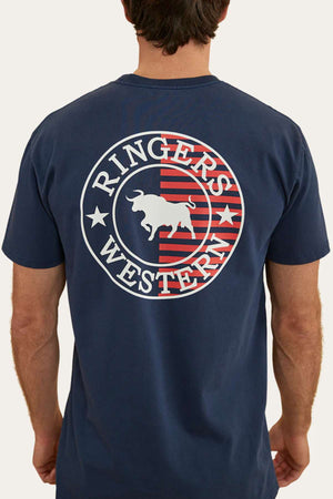 A person with short brown hair is seen from behind, wearing a dark blue Ringers Western Signature Flag Stock Fit T-Shirt made from 100% cotton. The t-shirt features a circular logo with a bull in the center and 'Ringers Western' written on it, accompanied by red and white stripes in the background.