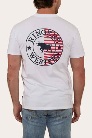 A man sporting the Ringers Western Signature Flag Stock Fit T-Shirt, adorned with "Ringers Western" and a bull logo on the back, showcases a circular emblem with red stripes. He pairs it perfectly with blue jeans, effortlessly embodying casual style.