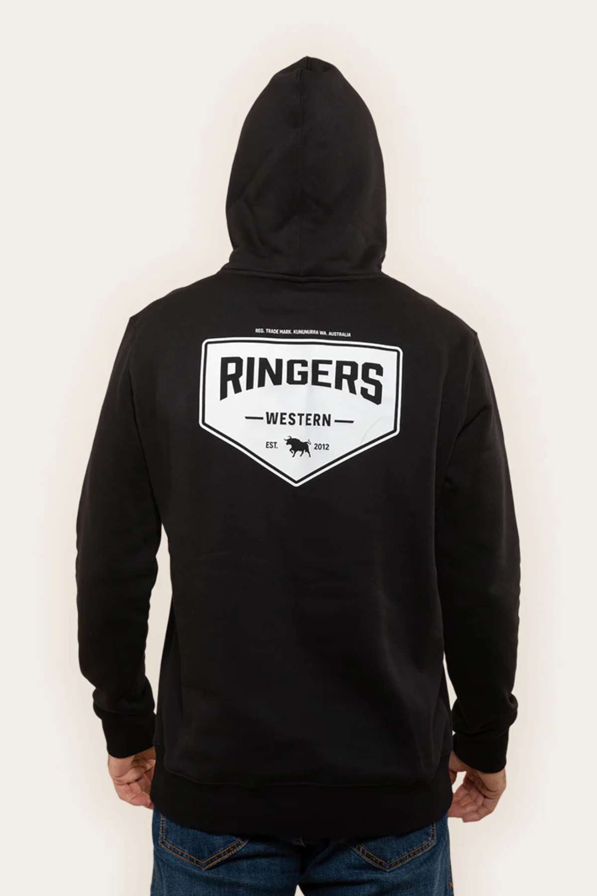 A person is shown from the back wearing the Ringers Western Squadron Hoodie in black. The hoodie features a white logo on the back that says "Ringers Western" along with an illustration of a bull's head and the text "Est 2012." Crafted from brushed fleece, it includes a cozy kangaroo pocket. The person is also wearing blue jeans.